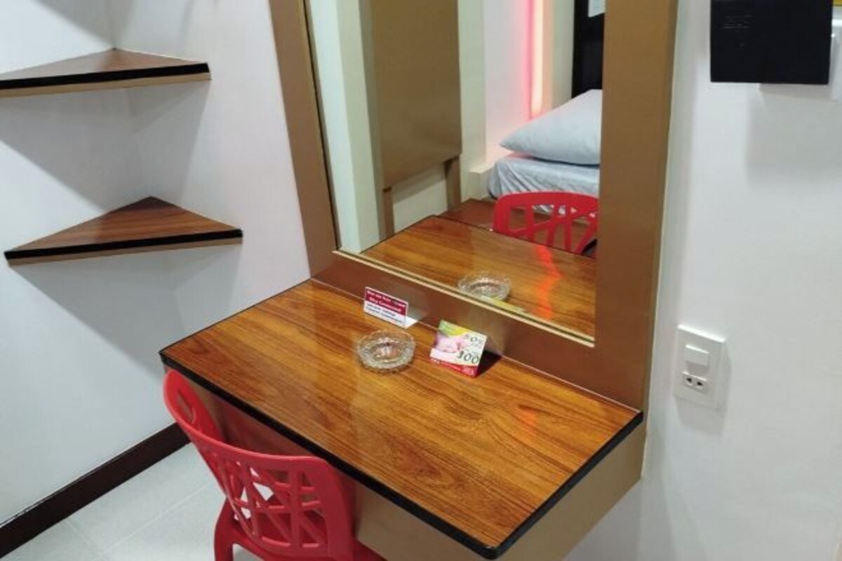 A small room with a wooden desk, a red chair, a mirror, and a bed with a blue pillow.