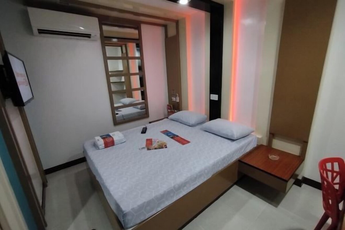 A small bedroom with a bed, a mirror, a red chair, and a wooden bench.