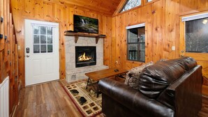 A cozy cabin interior with a stone fireplace, wooden walls, a leather couch, and a television. - River Ridge: Where Water Meets the Mountains (Pigeon Forge)