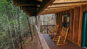 A wooden porch with two rocking chairs, surrounded by a forest. - River Ridge: Where Water Meets the Mountains (Pigeon Forge)