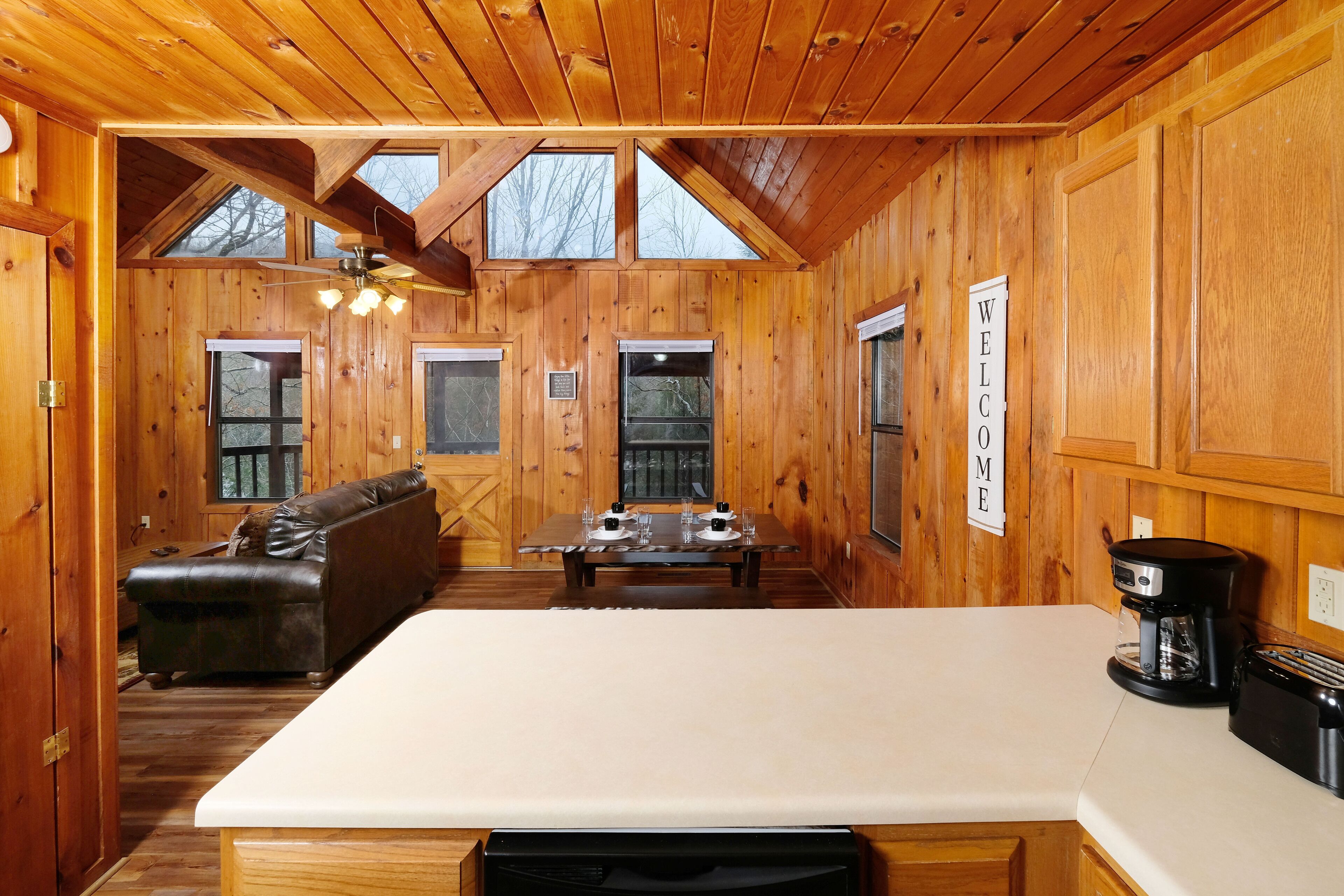 Ein Holzblockhaus-Interieur mit einem Esstisch, gedeckt für vier Personen, einer Couch, einer Kaffeemaschine und einem Schild mit der Aufschrift 'WELCOME'.