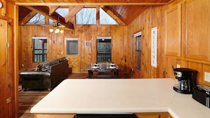 A wooden cabin interior with a dining table set for four, a sofa, a coffee maker, and a sign that reads "WELCOME". - River Ridge: Where Water Meets the Mountains (Pigeon Forge)