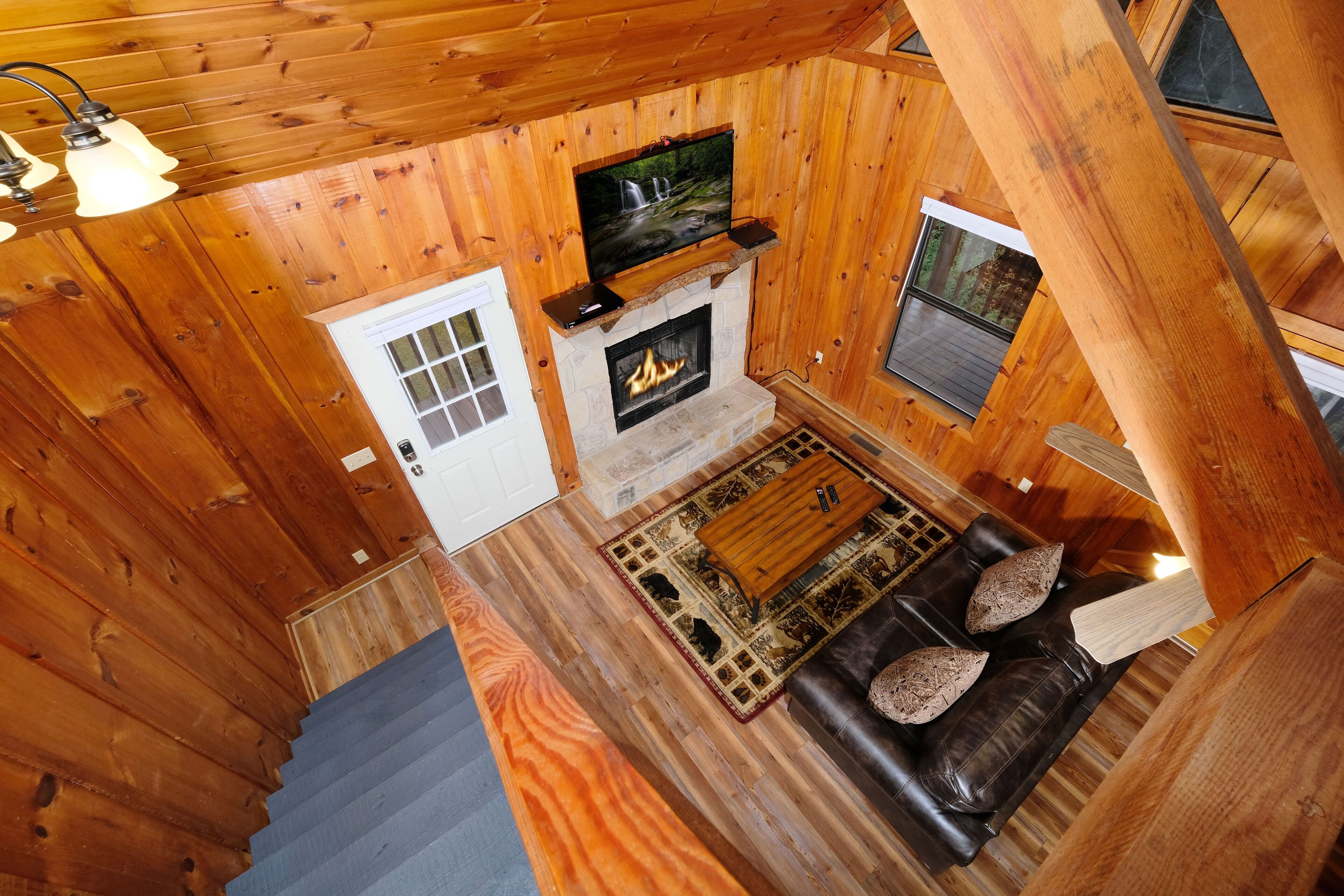 A cozy cabin interior with a fireplace, a leather sofa, and a television mounted above it.