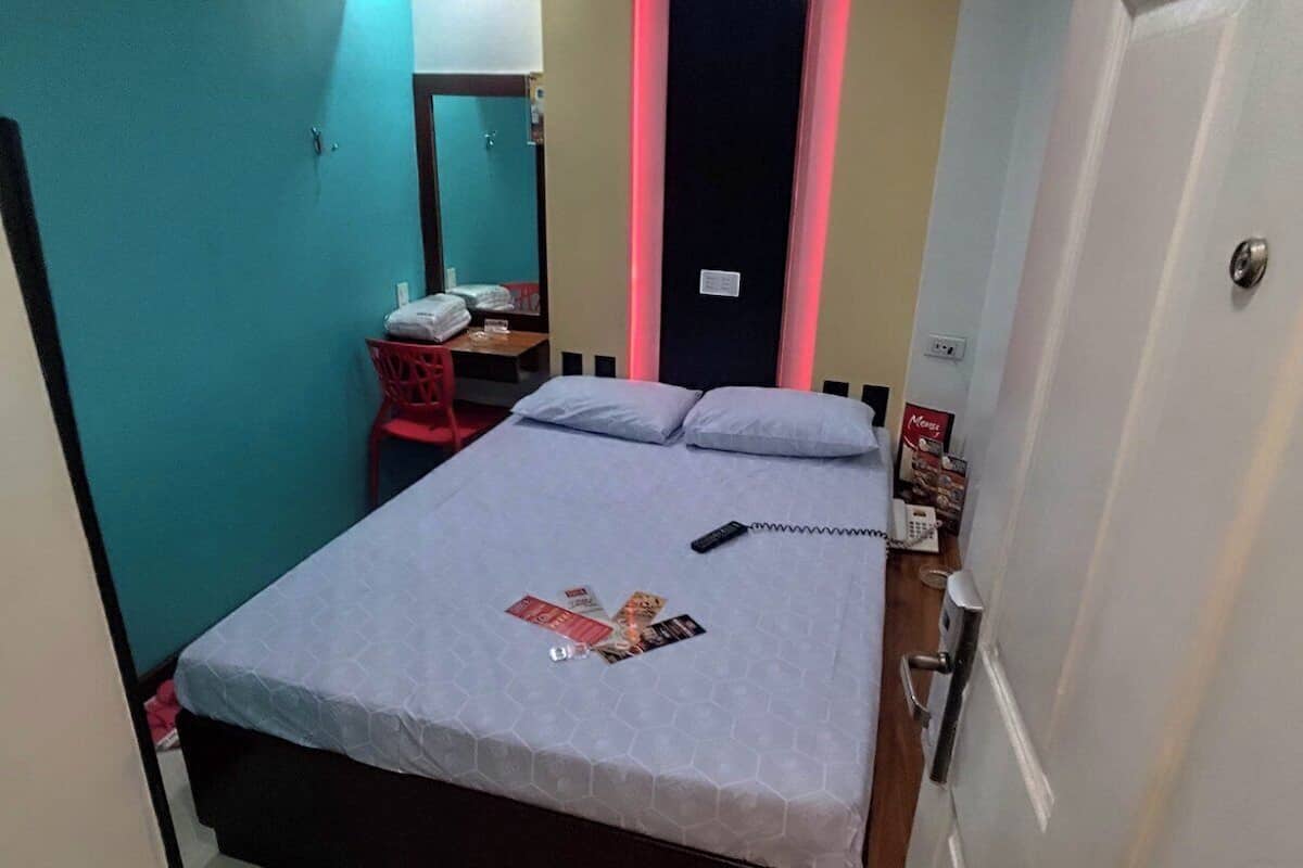 A bedroom with a bed, a desk, and an air conditioning unit.