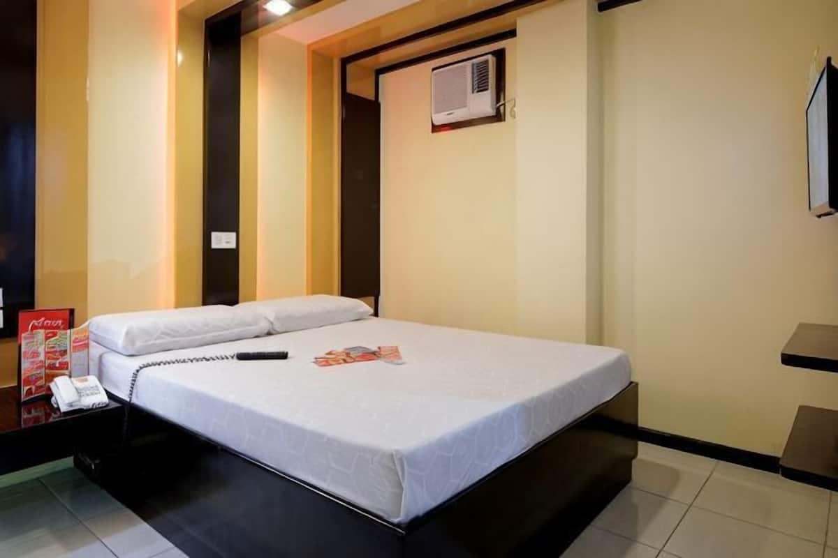 A hotel room with a bed, a bedside telephone, a wall-mounted air conditioner, and a small table.