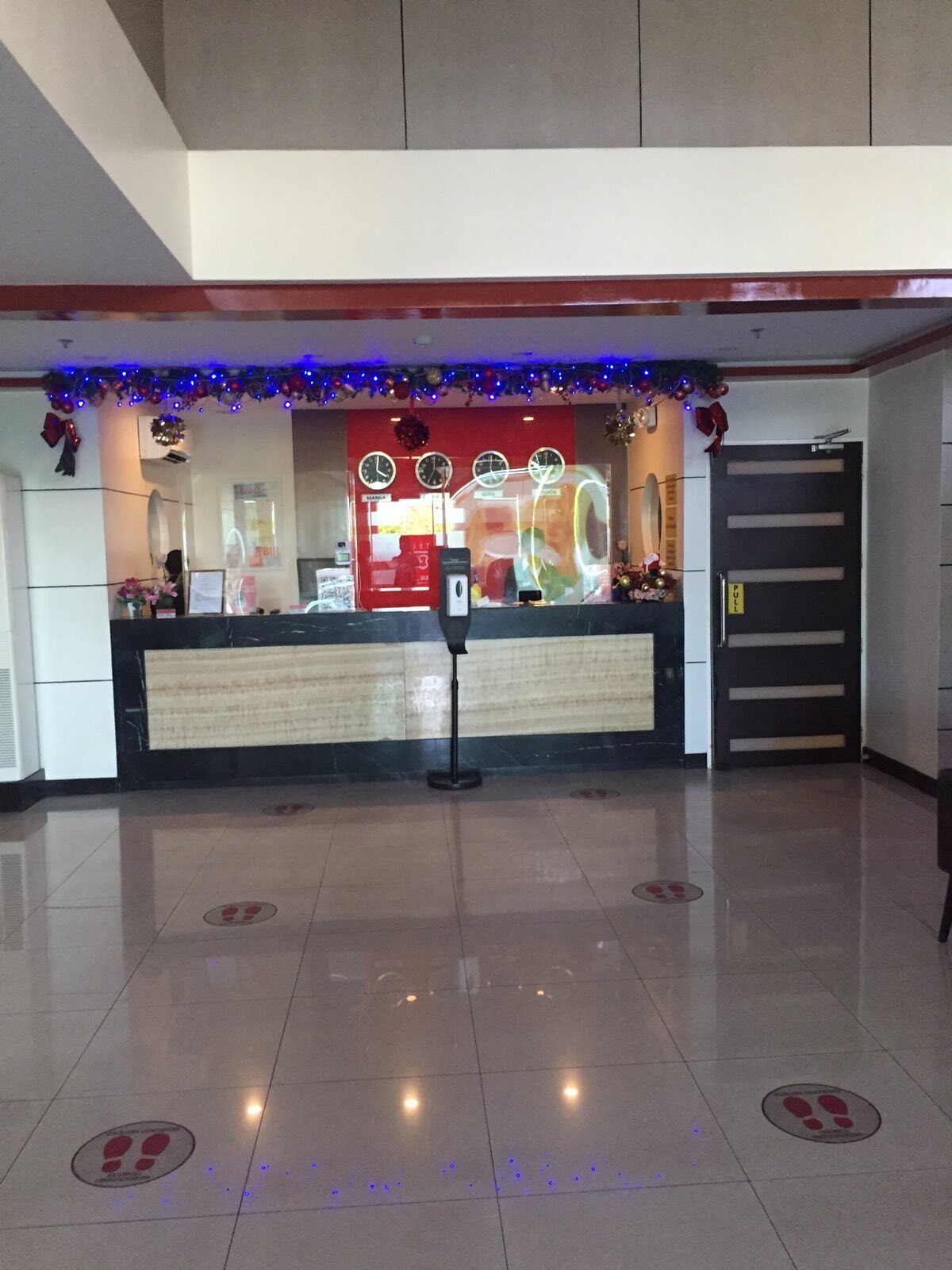 A hotel reception area with a counter, clocks, and a door.