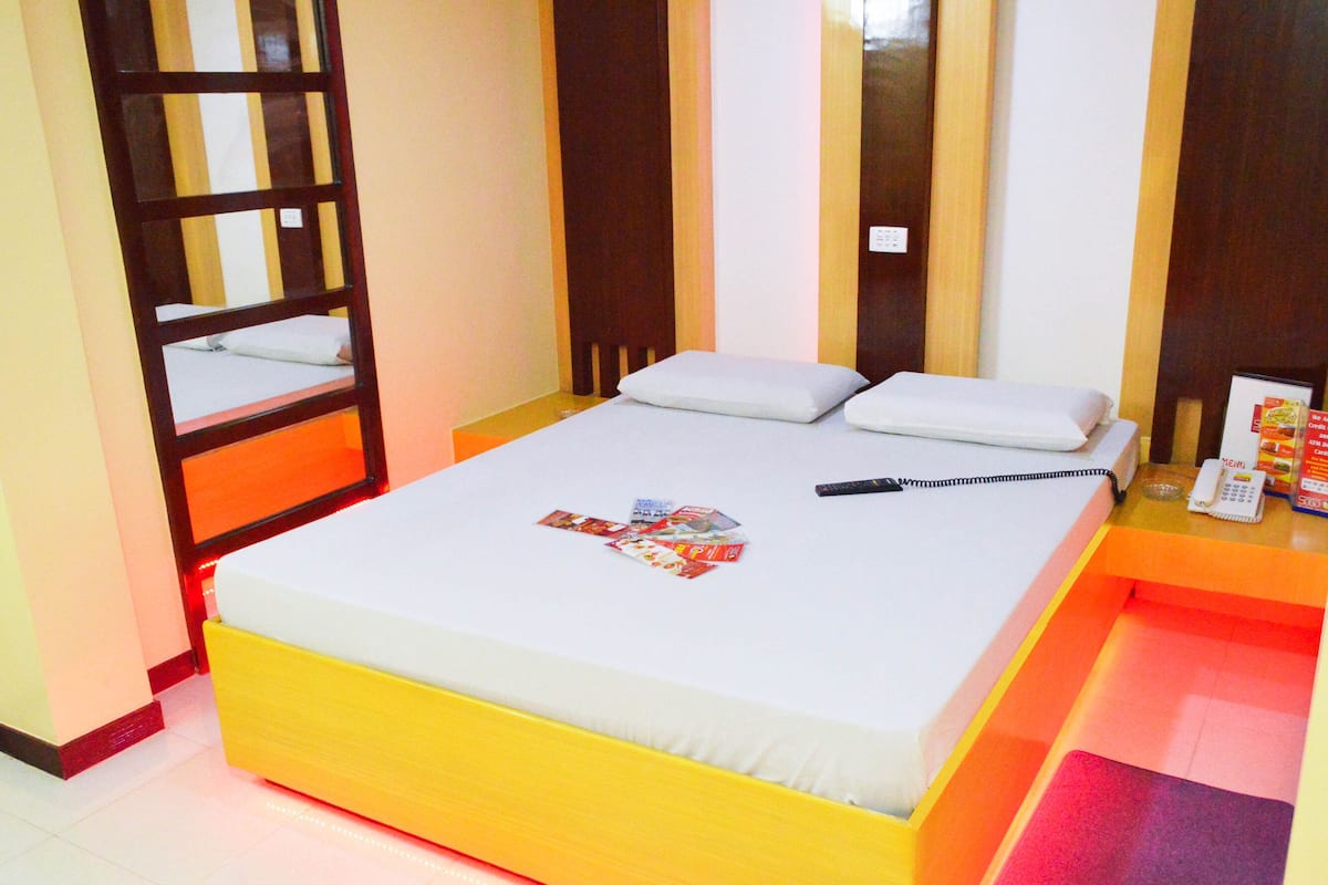 A hotel room with a bed, a bedside table with a phone and a menu, a mirror, and a door with a striped pattern.