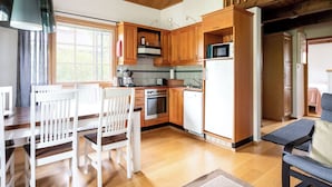 A modern kitchen with wooden cabinets, a stove, and a microwave. There is a dining area with white chairs and a table. - Tahkon klubitie 2 b by Interhome (Nilsiä)