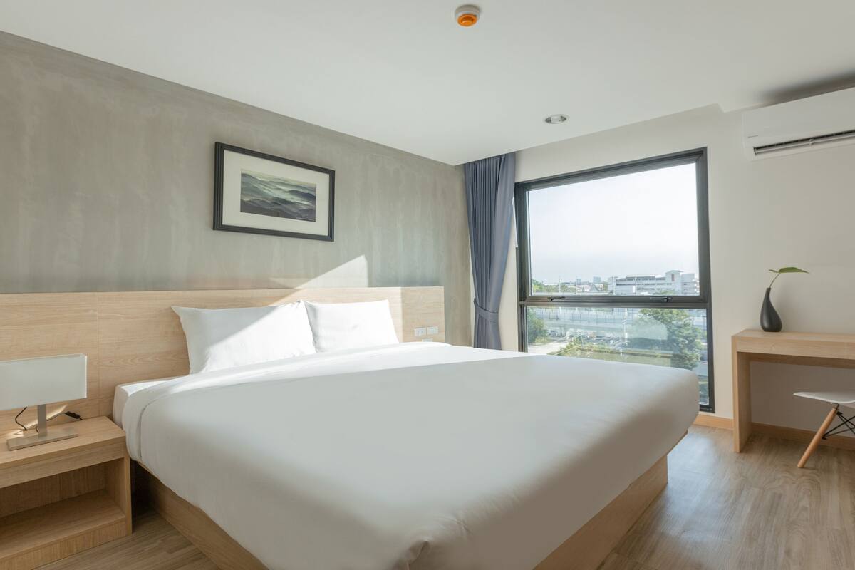 A modern hotel room with a large bed, a desk, and a window offering a city view.