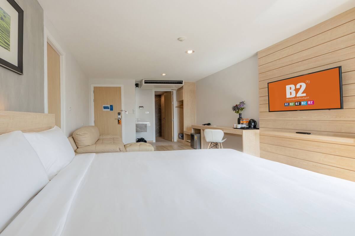 A hotel room with a large bed, a desk, a chair, and a TV on the wall.