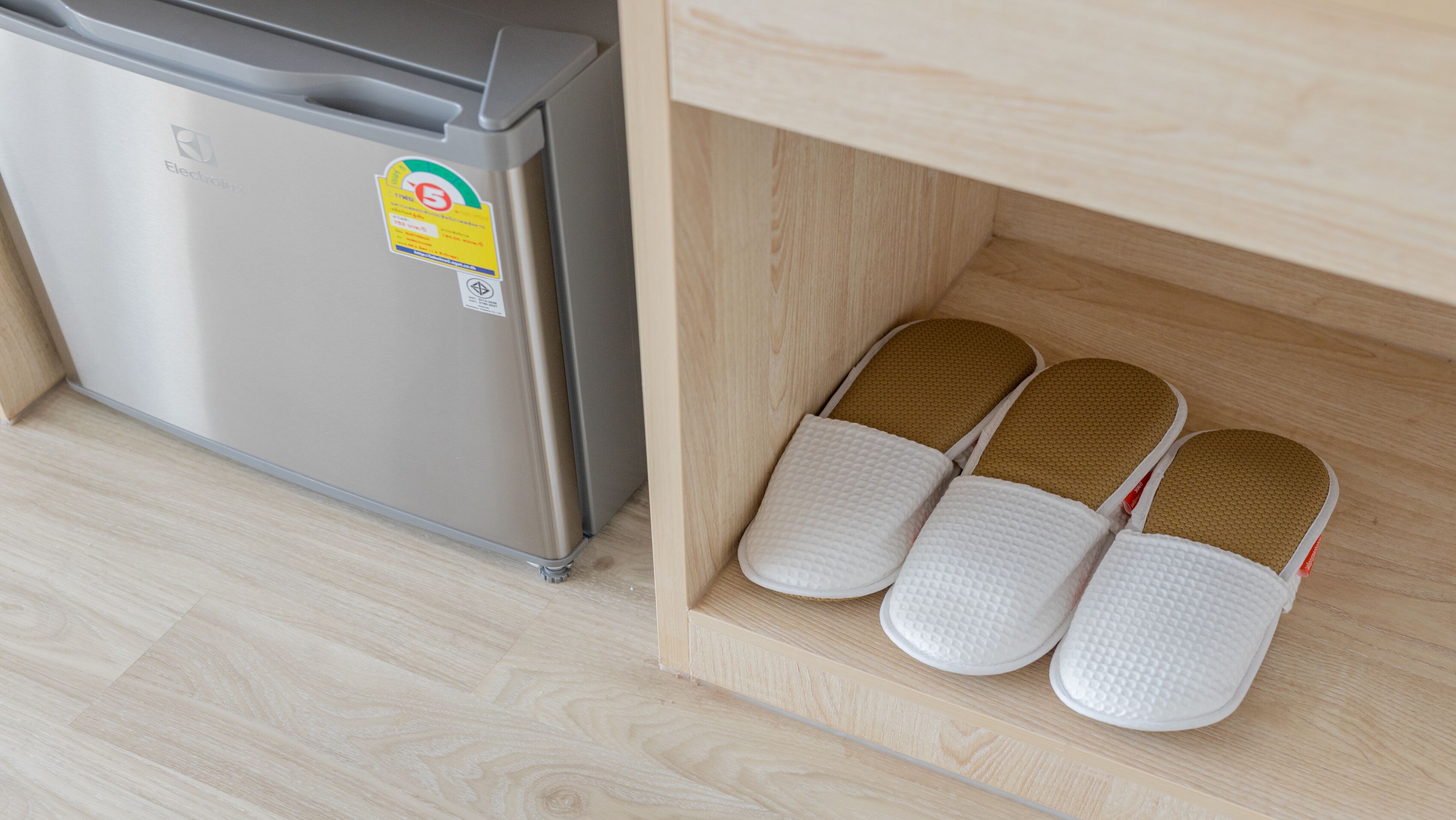 A kitchen with a stainless steel refrigerator and a wooden cabinet with slippers.