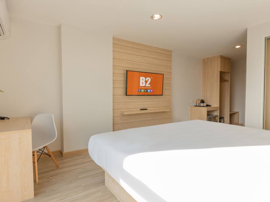 A modern hotel room with a bed, a desk, a chair, a TV mounted on the wall, and a wardrobe.