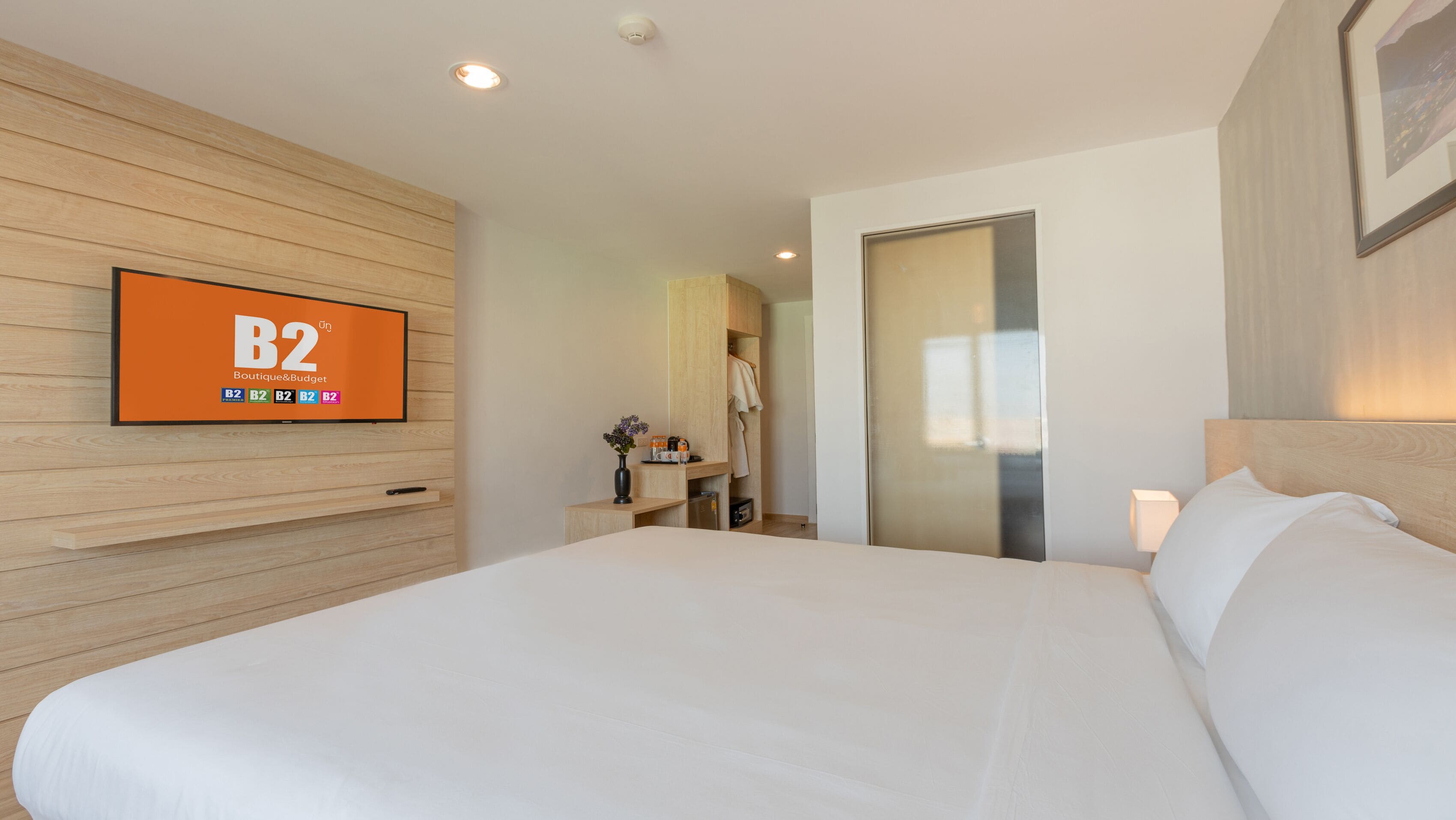 Une chambre d’hôtel avec un grand lit, un téléviseur fixé au mur, un mur recouvert de panneaux en bois, une armoire et une porte de salle de bain.
