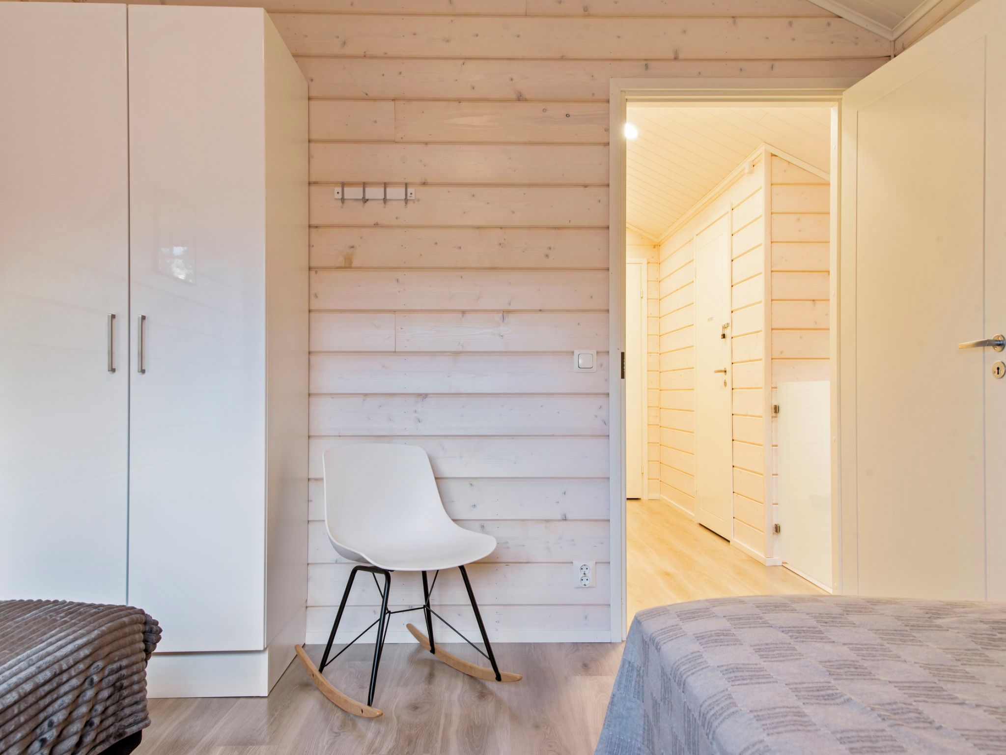 Une pièce avec une armoire blanche, une chaise blanche et un lit recouvert d’une couvre-lit à motifs.