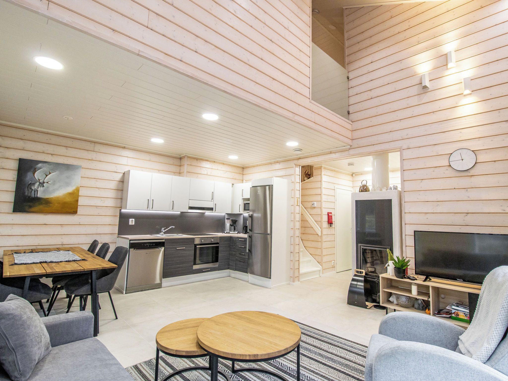 Une cuisine moderne équipée d’appareils électroménagers en acier inoxydable, un coin repas avec une table et des chaises en bois, et un salon avec un téléviseur et des fauteuils.