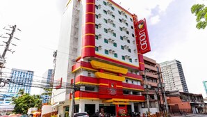 Een hotel met meerdere verdiepingen, een opvallende gevel in rood en geel, diverse balkons en een duidelijk herkenbaar bord dat het een hotel is.