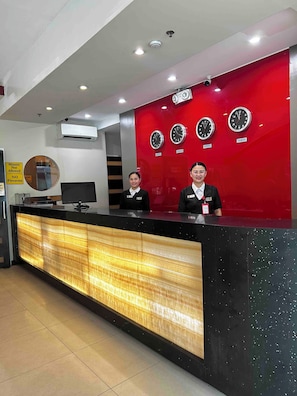 A reception desk with a red wall featuring clocks labeled with city names. - Hotel Sogo Mindanao Ave. (Quezon City)