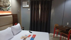 Een hotelkamer met een bed, een bureau, een stoel, een wandairconditioner en een gordijn.