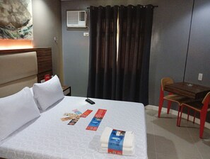 A hotel room with a bed, a desk, a chair, a wall-mounted air conditioner, and a curtain.
