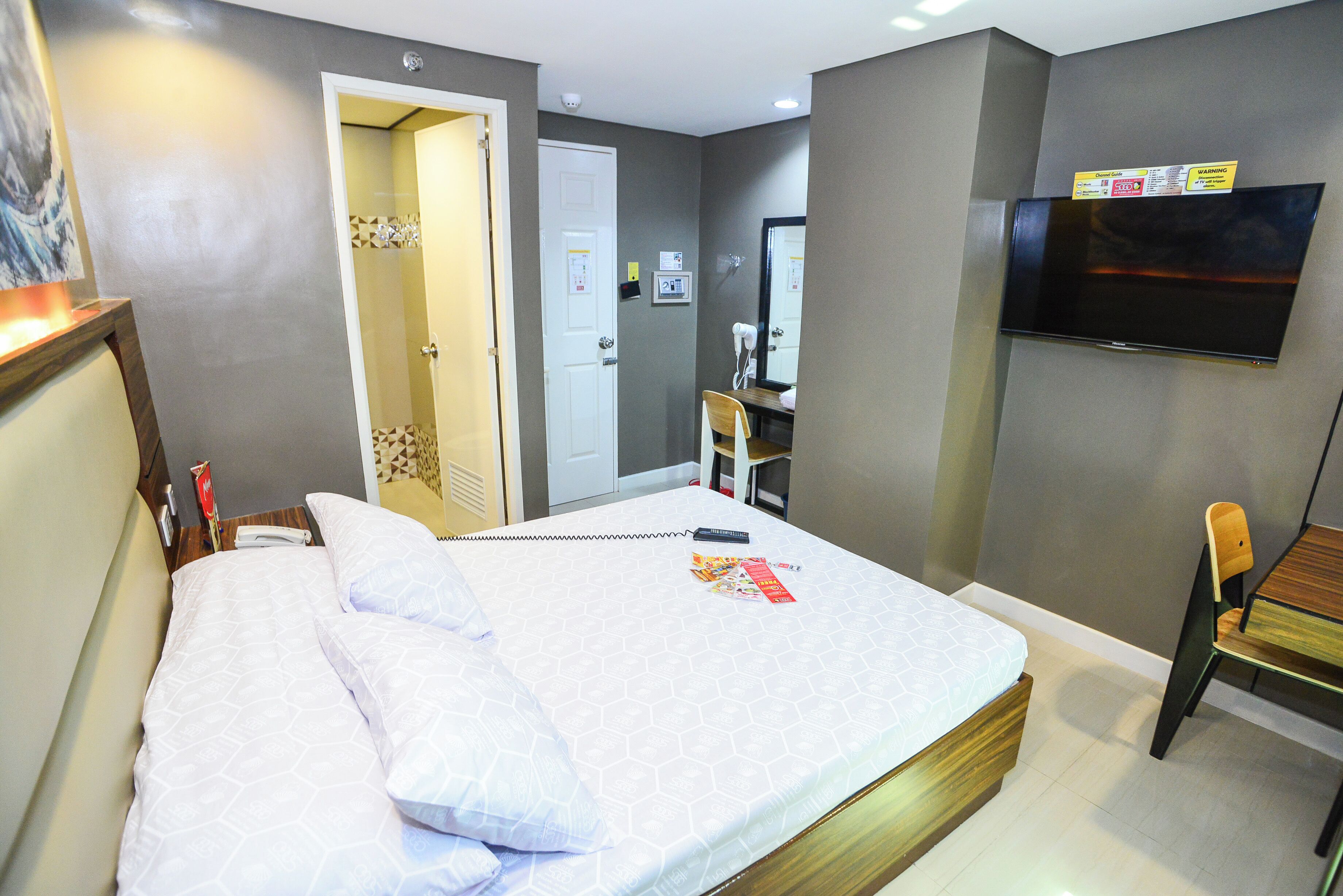 A hotel room with a bed, a desk, a chair, a TV, and a bathroom door.