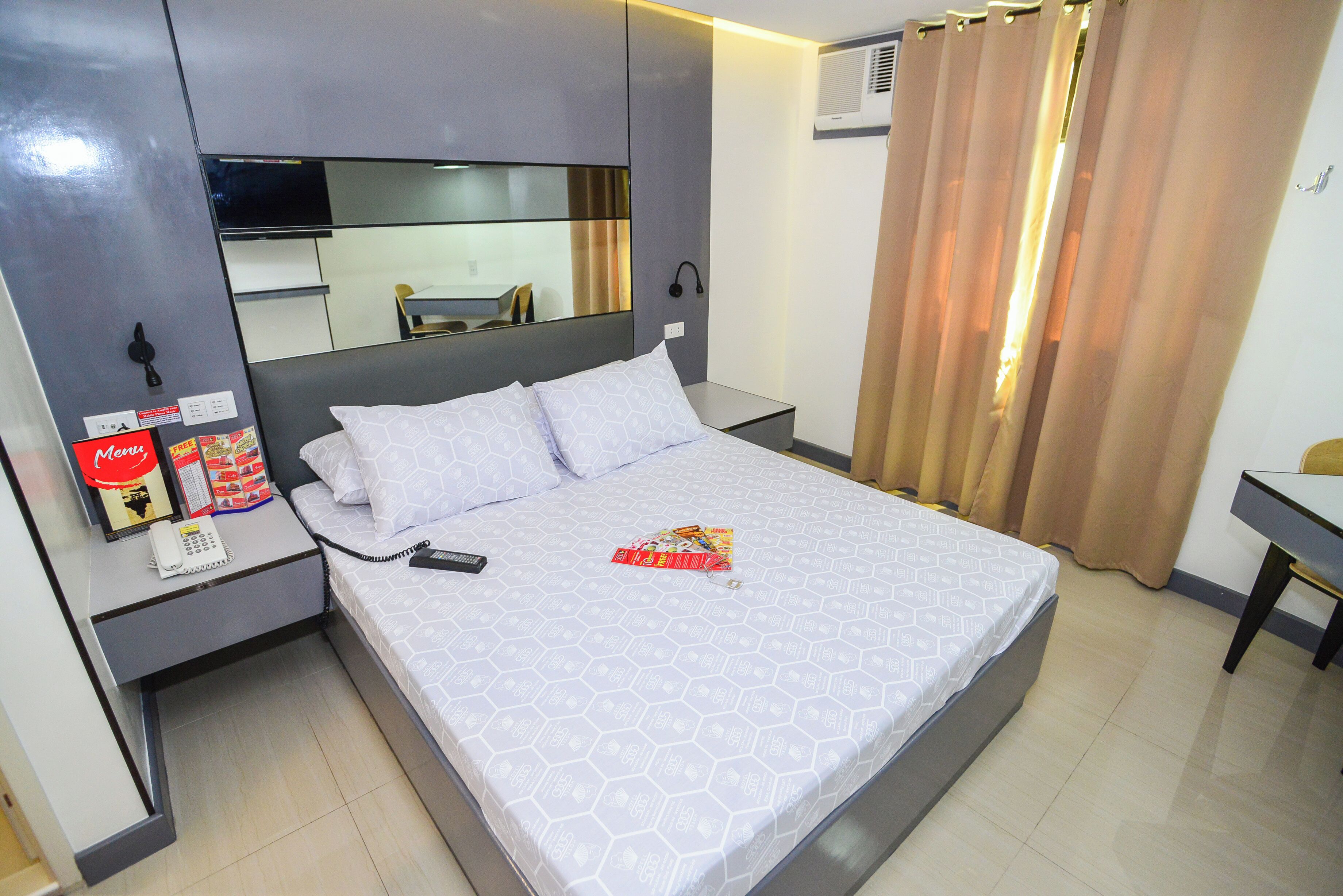 A hotel room with a bed, bedside table, a mirror, a desk, and a chair.
