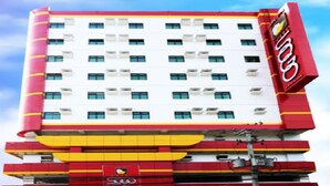 Een hotel met meerdere verdiepingen, met een rood en wit gevel, en een opvallend logo aan de rechterkant.