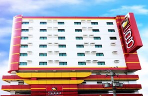 A multi-story hotel with a red and white facade, featuring a prominent logo on the right side.
