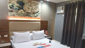 Hotelkamer met een groot bed, hoofdeinde, nachtkastje met telefoon en tijdschrift, wandairconditioning en gordijn.