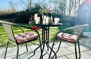 A round table with two chairs, a coffee pot, and two cups on a patio with a grassy background and trees. - Doppelzimmer 23 - Strandhaus Mönchgut (Mönchgut)