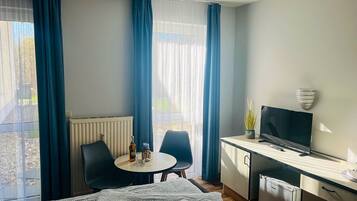 Ein Hotelzimmer mit einem Bett, einem Schreibtisch mit Fernseher, einem kleinen Tisch mit einer Flasche, zwei Stühlen und einem Heizkörper.