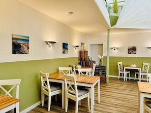 A dining area with wooden tables and white chairs, green walls, and wall-mounted lights. - Doppelzimmer 24 - Strandhaus Mönchgut (Mönchgut)