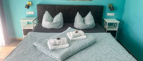 Un dormitorio con cama, dos mesitas de noche, una lámpara de pared, un cuadro y vistas a la playa.