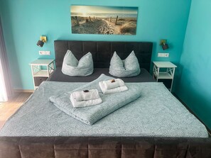 A bedroom with a bed, two nightstands, a wall-mounted lamp, a painting, and a view of the beach. - Doppelzimmer 24 - Strandhaus Mönchgut (Mönchgut)