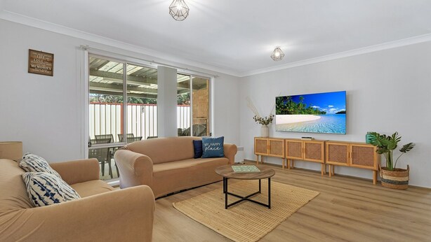 A living room with a beige sofa, a coffee table, and a TV on the wall.
