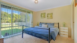A bedroom with a bed, bedside tables, and a view of a garden through large windows.