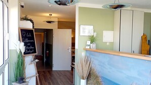 A reception area with a wooden floor, a reception desk, a chalkboard with a welcome message, a potted plant, and a painting of a beach scene. - Doppelzimmer 25 - Strandhaus Mönchgut (Mönchgut)