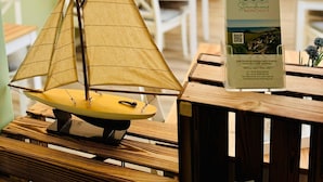 A model sailboat on a wooden table, a signboard with hotel information, and a dining area with tables and chairs. - Doppelzimmer 25 - Strandhaus Mönchgut (Mönchgut)