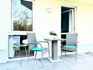 Two wicker chairs with teal cushions, a small table, and a potted plant on a balcony with a view of trees. - Doppelzimmer 25 - Strandhaus Mönchgut (Mönchgut)
