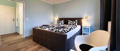 A bedroom with a bed, bedside table, chair, and a door leading to another room.
