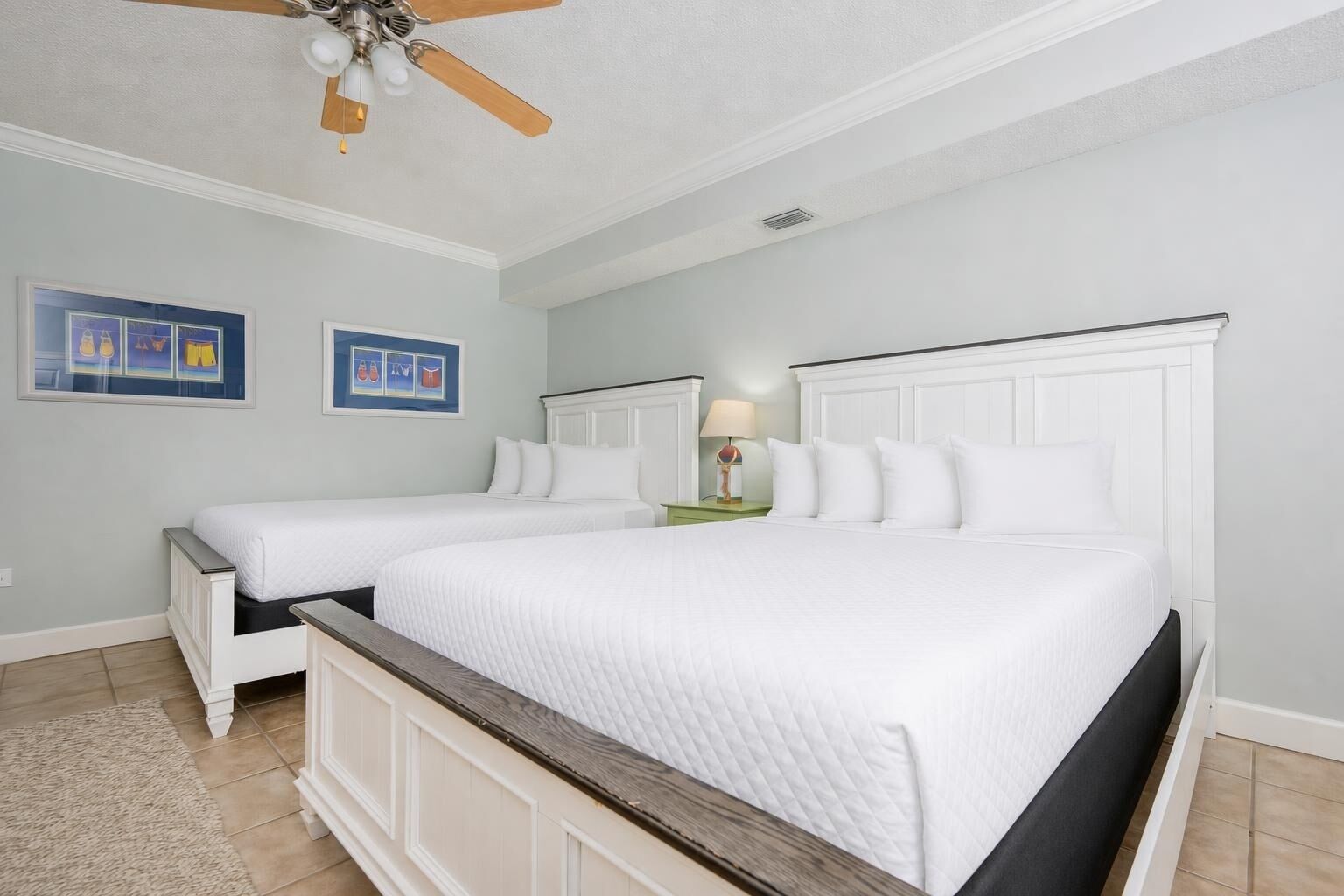 A bedroom with two beds, a ceiling fan, and artwork on the walls.