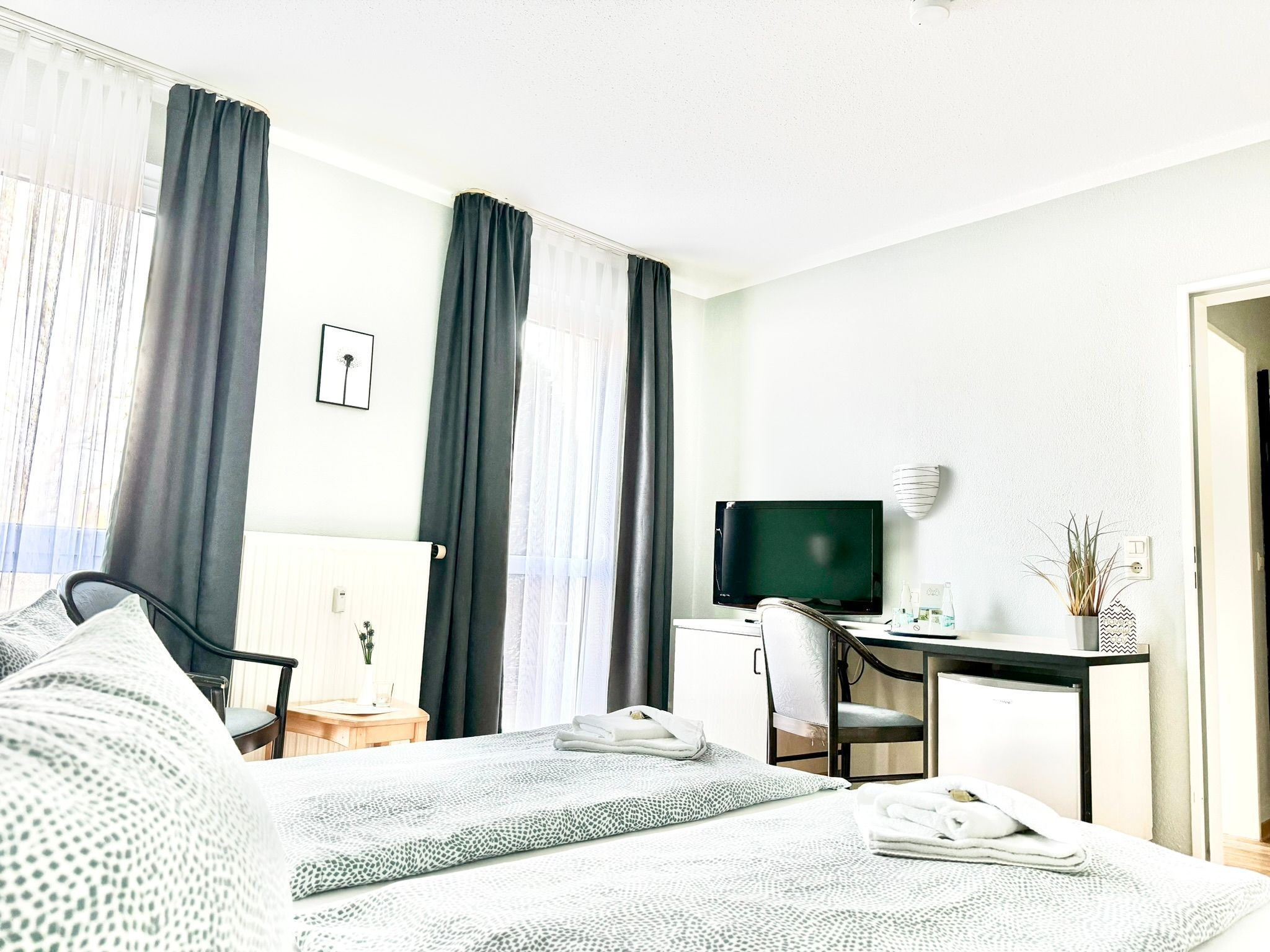 Ein Hotelzimmer mit Bett, Schreibtisch, Sessel, Fernseher und einem kleinen Tisch mit Pflanze.