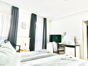 A hotel room with a bed, a desk, a chair, a television, and a small table with a plant. - Doppelzimmer 28 - Strandhaus Mönchgut (Mönchgut)