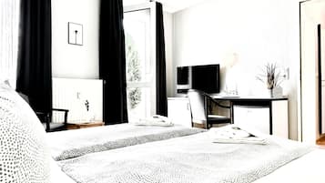 Ein Hotelzimmer mit einem Bett, einem Schreibtisch mit Fernseher, einem Sessel und einem Fenster mit Vorhängen.
