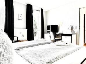A hotel room with a bed, a desk with a TV, a chair, and a window with curtains. - Doppelzimmer 28 - Strandhaus Mönchgut (Mönchgut)