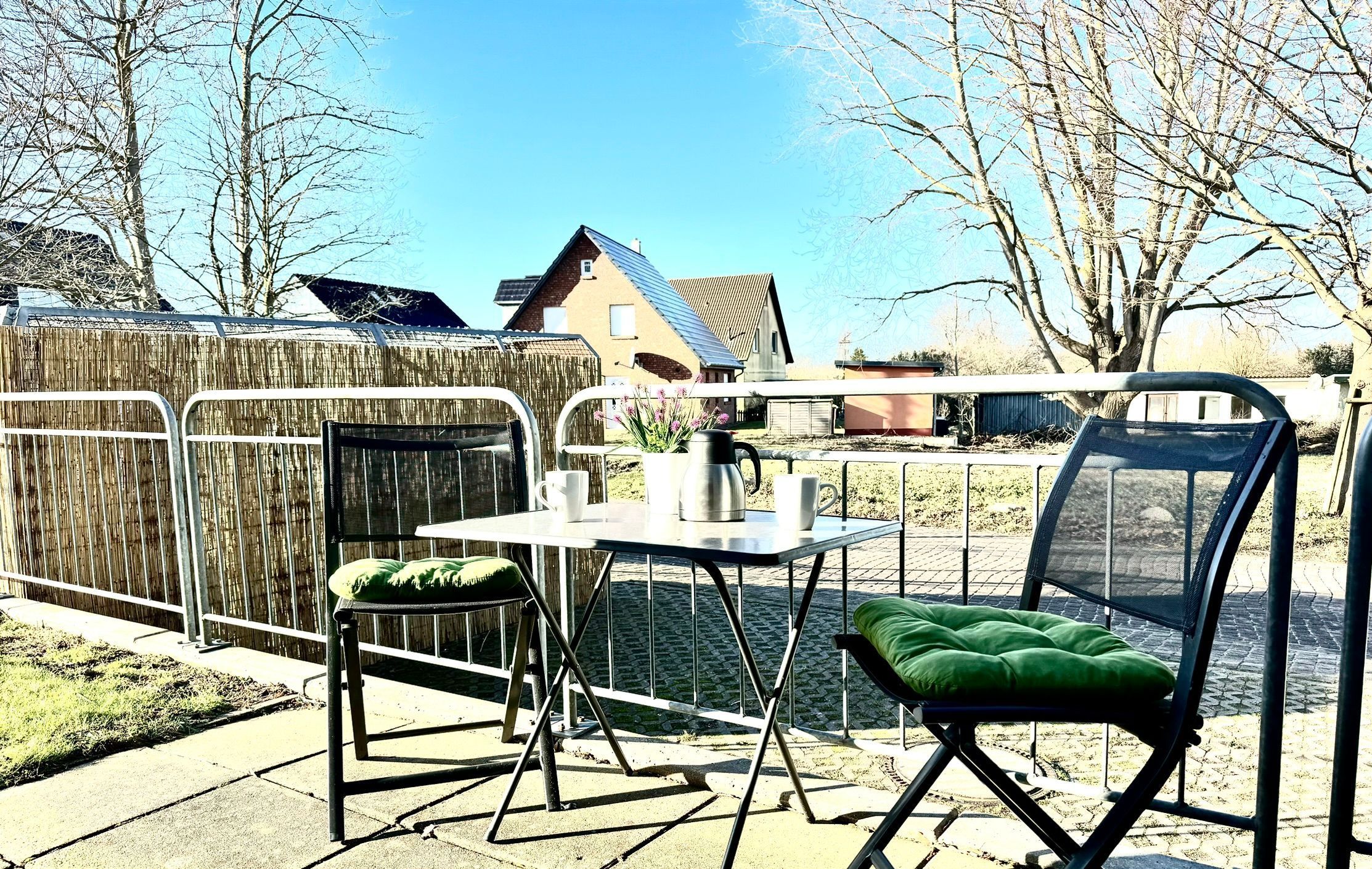 A patio with a table and chairs, a wooden fence, and a house in the background.