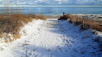 Un sendero cubierto de nieve que lleva a una playa, con vistas despejadas al océano y un cielo nublado.
