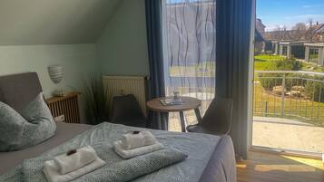 Ein Hotelzimmer mit Bett, einem kleinen Tisch, Stühlen, Blick ins Freie und einem Balkon.