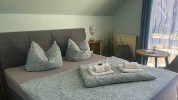 Ein Schlafzimmer mit Bett, Kissen, einem Nachttisch und Blick ins Freie.