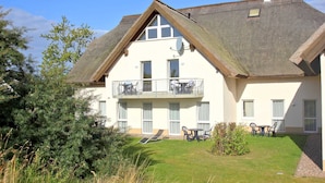 A two-story building with a balcony, a small garden, and a thatched roof. - Doppelzimmer 33 - Strandhaus Mönchgut (Mönchgut)