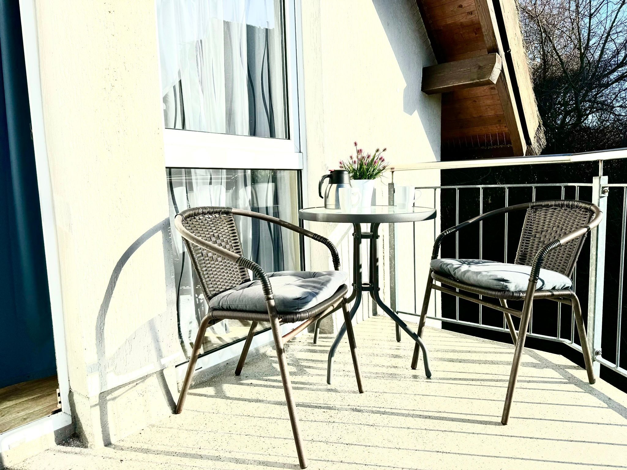 Un balcon avec deux fauteuils en osier, une petite table ronde et un pot de fleurs.